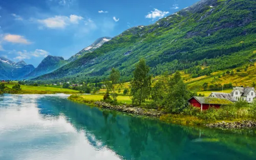 Flusslandschaft mit Bergen, grünen Wiesen, roten Häusern und blauem Himmel.