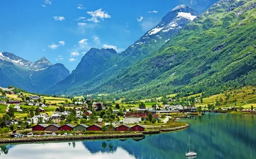 Norwegisches Fjorddorf mit Bergen und Häusern am Ufer, segelndes Boot im Wasser.