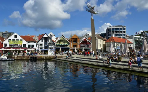 Hafenpromenade mit bunten Häusern und Menschen am Wasser bei sonnigem Wetter.