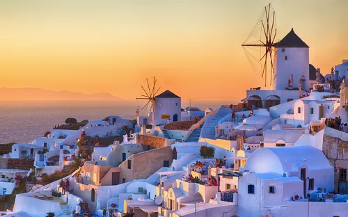 Stadtansicht von Santorini bei Sonnenuntergang mit Windmühlen und weißen Gebäuden.