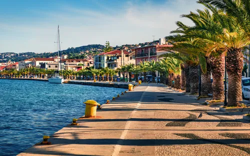 Promenade mit Palmen entlang des Wassers und Gebäuden im Hintergrund.