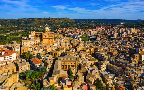Luftaufnahme einer mediterranen Stadt mit Hügeln im Hintergrund.