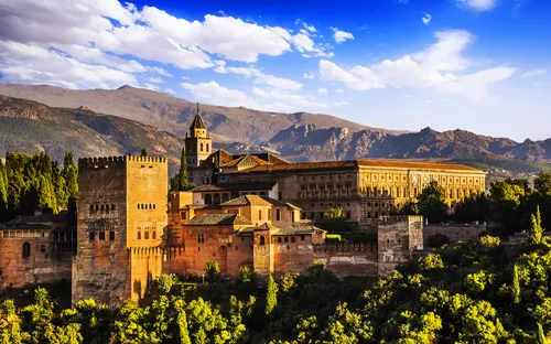 Alhambra in Granada vor einer Bergkulisse bei strahlendem Sonnenschein.