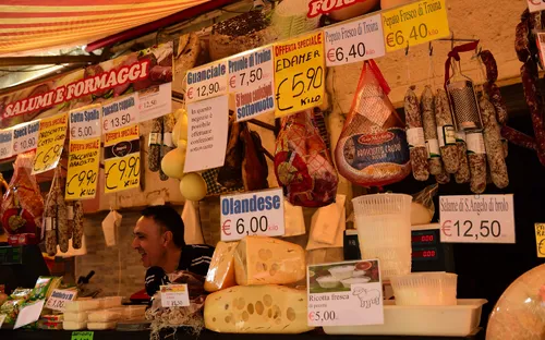Marktstand mit italienischen Wurst- und Käsesorten, Verkaufsschilder und Preise sichtbar.