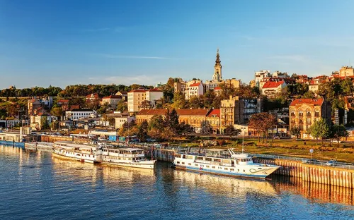 Ein Fluss mit mehreren Booten am Ufer und eine Stadtansicht im Hintergrund bei Sonnenuntergang.