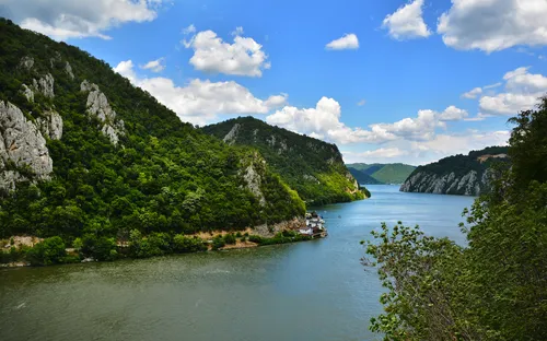 Fluss in einer Berglandschaft mit grünem Wald und blauem Himmel.
