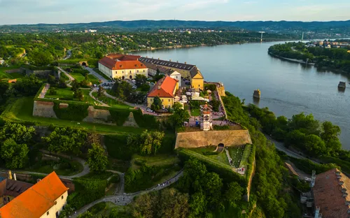 Luftaufnahme einer Festung an einem Fluss mit grüner Umgebung und besiedeltem Hintergrund.