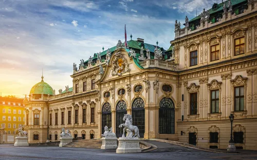 Barocker Palast bei Sonnenuntergang mit weißen Statuen im Vordergrund.