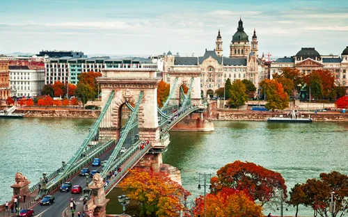 Historische Kettenbrücke über Fluss mit Stadt im Hintergrund.